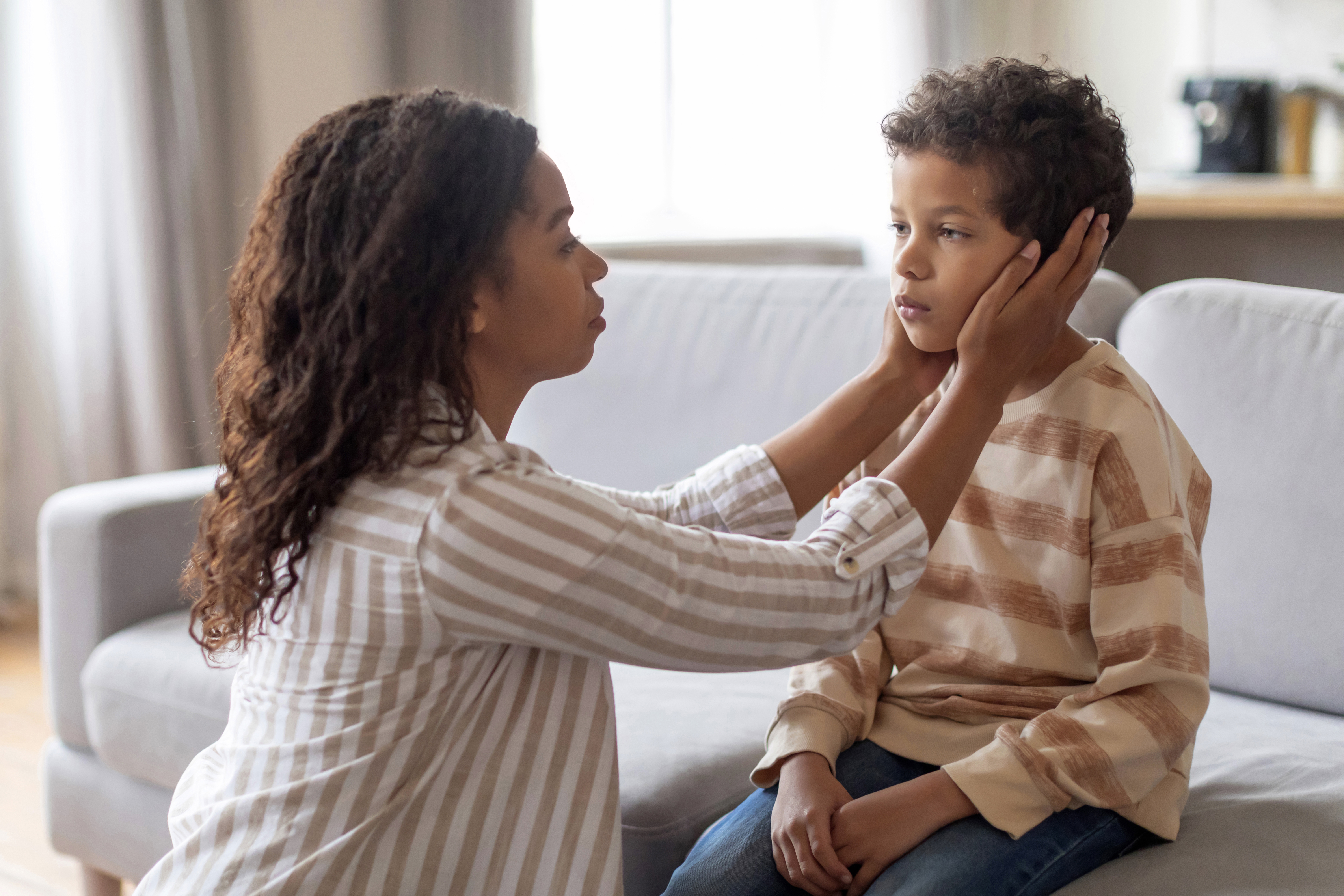 A concerned mother tenderly holding her son's face at home