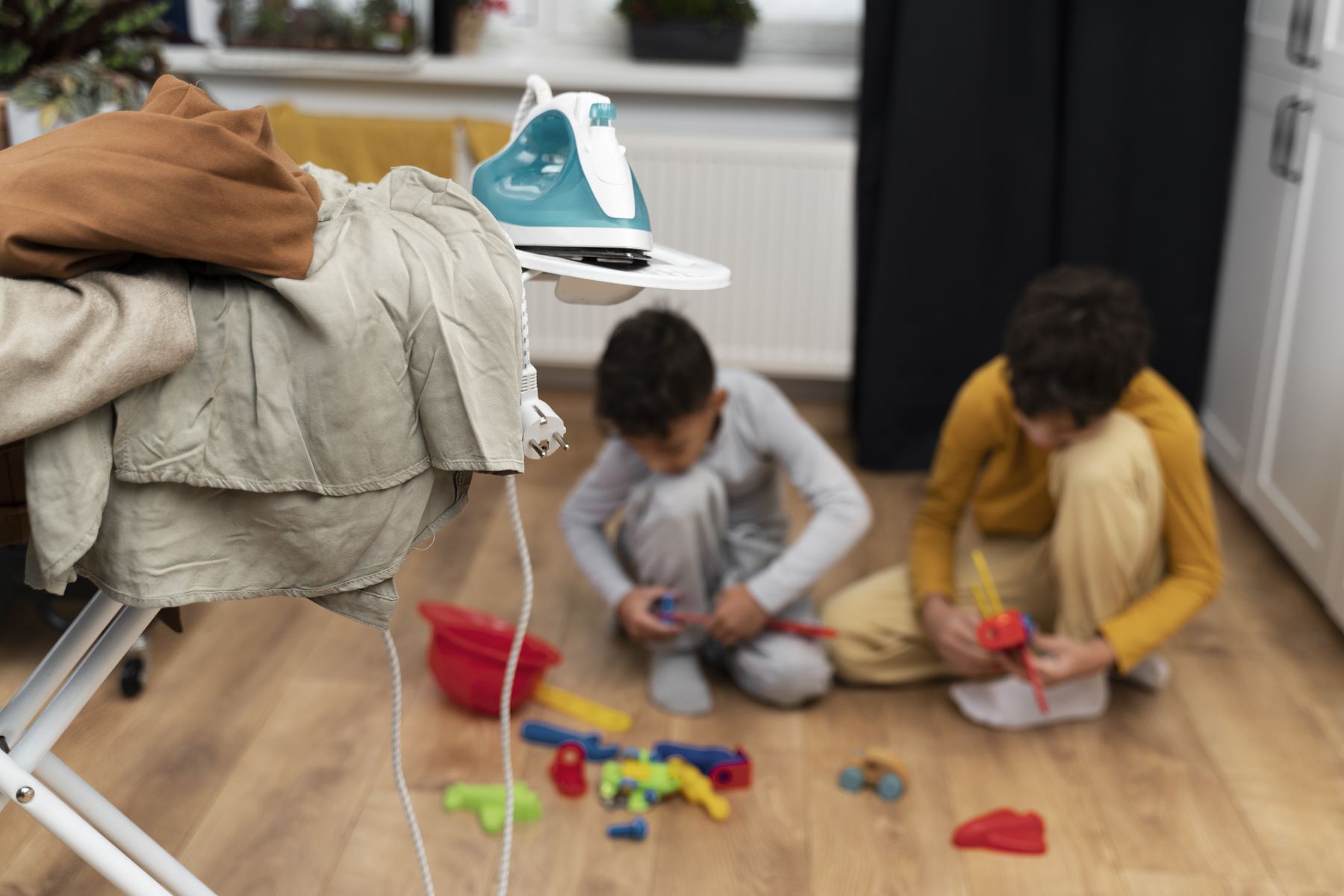 Two children playing on the floor surrounded by laundry and toys