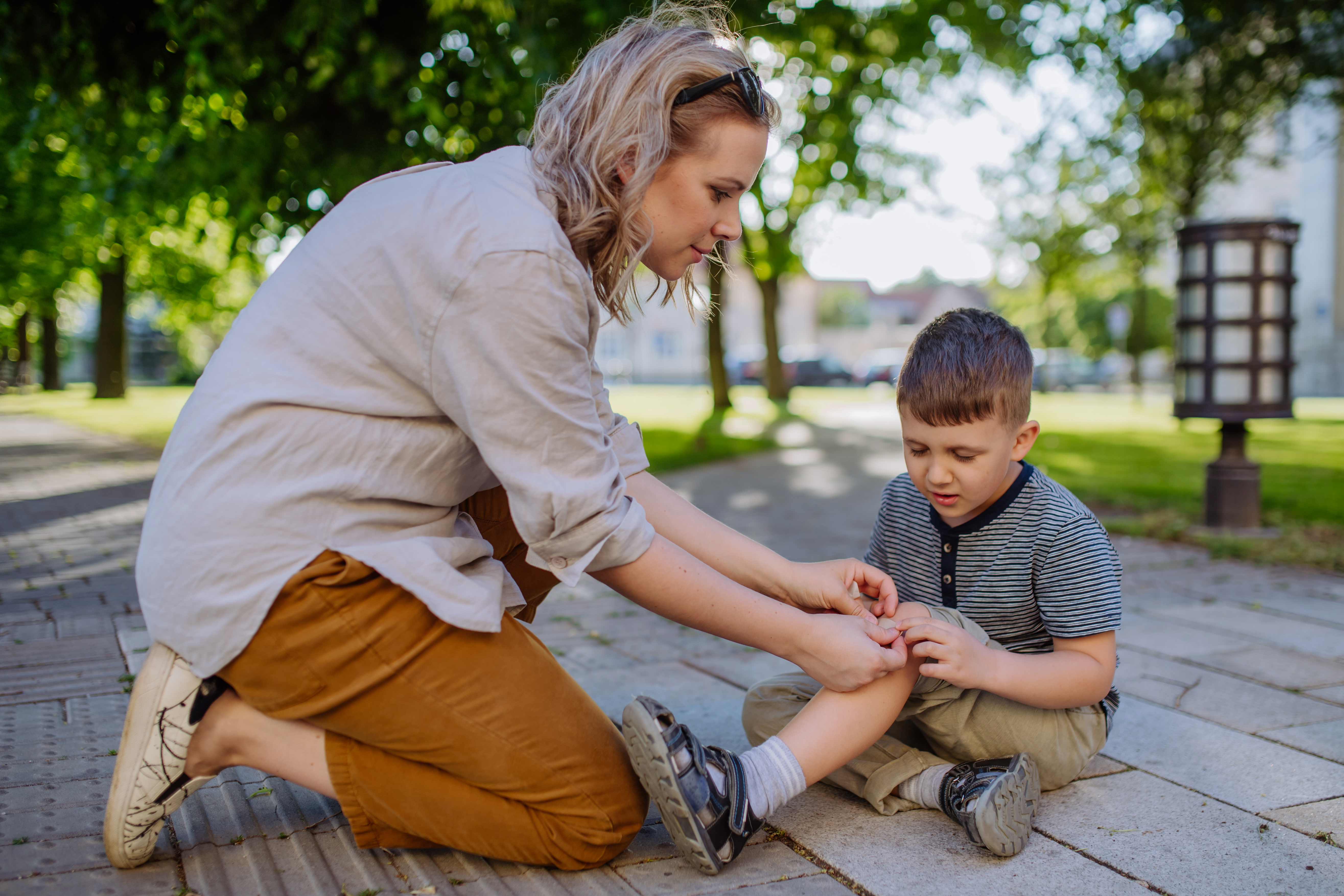 A young mother kneels on the sidewalk and tends to her son's scraped knee