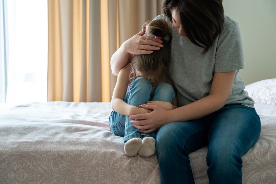 A mother comforting her young daughter on a bed at home